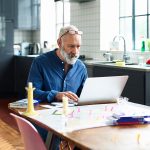 Eine Person sitzt an einem Tisch in einer Wohn- und Essk&uuml;che und blickt in einen aufgeklappten Laptop.