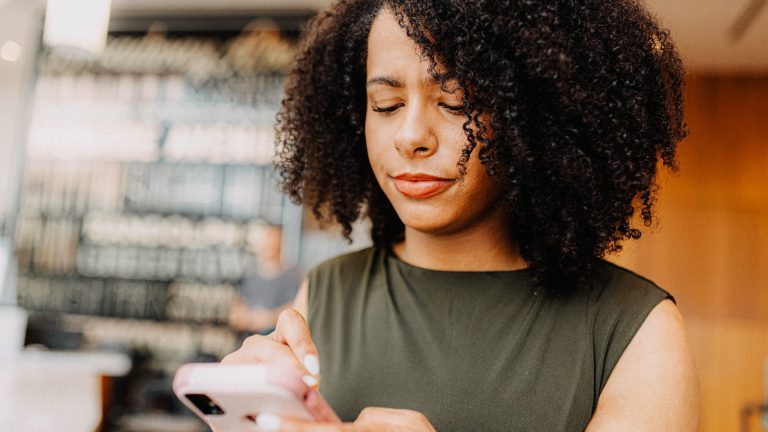 Eine Person h&auml;lt ihr Smartphone in den H&auml;nden auf das sie skeptisch blickt.