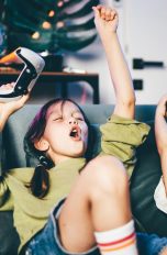 PlayStation Family-App, Kindersicherung und mehr nutzen Zwei Kinder mit Dualsense-Controllern sitzen auf einem Sofa und reißen die Arme freudig in die Luft.