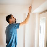 Eine Person steht vor einem Fenstersturz, ber&uuml;hrt diesen mit der Hand und wirft darauf einen kontrollierenden Blick.