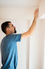 Schimmel vermeiden und entfernen, So bleibt deine Wohnung schimmelfrei Eine Person steht vor einem Fenstersturz, berührt diesen mit der Hand und wirft darauf einen kontrollierenden Blick.