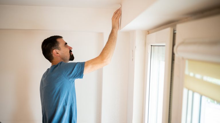 Eine Person steht vor einem Fenstersturz, ber&uuml;hrt diesen mit der Hand und wirft darauf einen kontrollierenden Blick.