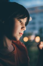 Fritzbox-Kindersicherung einrichten, So begrenzt du Internetzeiten Eine Person sitzt in einem dunklen Raum und blickt auf ein Smartphone.