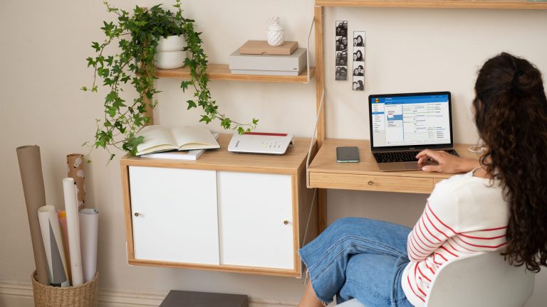 Eine Person sitzt auf einem Stuhl an einem Schreibtisch und arbeitet an einem Laptop.