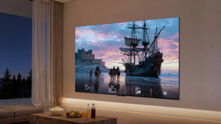 In einem Wohnzimmer ist ein Fernseher an der Wand montiert, auf dem Bildschirm ist ein altes Segelschiff zu sehen.