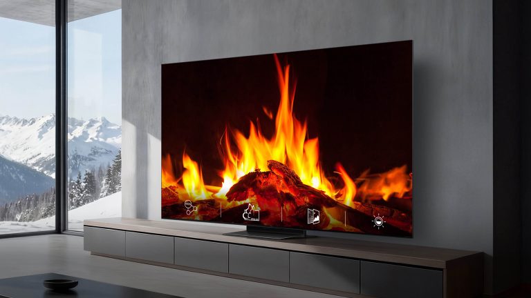 TCL-TV, Sendersuchlauf durchführen und Sender sortieren In einem modernen Wohnraum hängt ein großer Fernseher an der Wand, auf dem ein Kaminfeuer dargestellt wird. Im Hintergrund ist durch eine große Fensterfront eine verschneite Berglandschaft sichtbar.