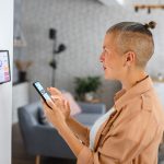 Eine Person steht mit einem Smartphone vor einem Tablet, mit dem die smarte Beleuchtung gesteuert wird.&nbsp;