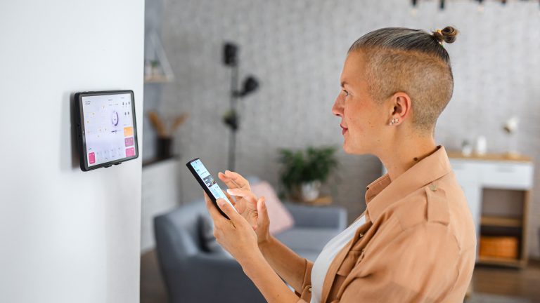 Eine Person steht mit einem Smartphone vor einem Tablet, mit dem die smarte Beleuchtung gesteuert wird.&nbsp;
