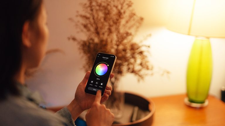 Smart Lights, So machst du deine Beleuchtung steuerbar Eine Person hält ein Smartphone in der Hand mit dem sie die Lichtfarbe einer Lampe steuert.