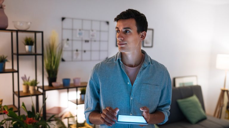 Eine Person steht mit einem Tablet in den H&auml;nden in einem Wohnzimmer.&nbsp;