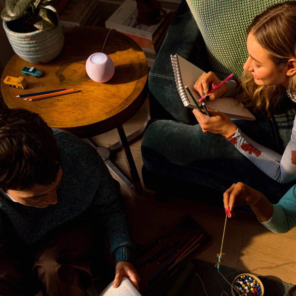Drei Personen sitzen und liegen um einen Tisch herum auf dem ein Apple HomePod steht.