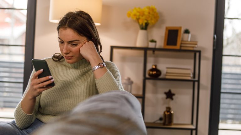 Eine Person schaut in einem Wohnraum auf ein Smartphone.