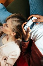 Cozy Gaming, Spiele und Zubehör für den Herbst Zwei Personen liegen gemütlich auf einem Sofa und halten Controller in der Hand.