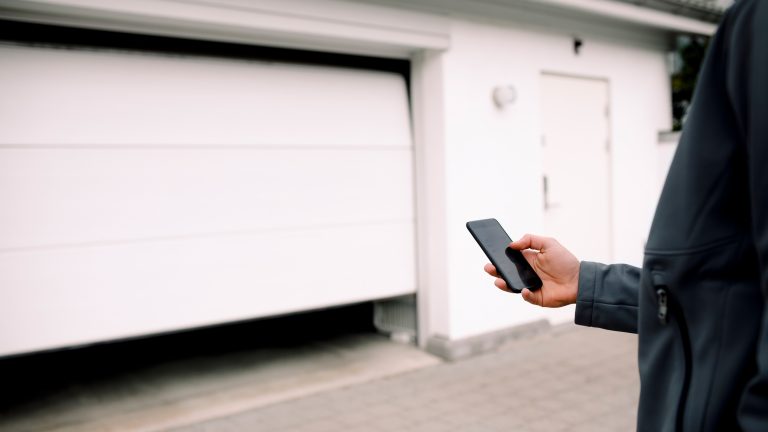 Eine Person hält ihr Smartphone in der Hand und scheint damit ein Garagentor zu öffnen.