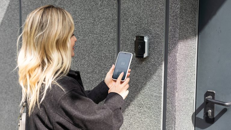 Smart-Home-Security, So schützt du dich vor Hackern Eine Person hält ihr Smartphone in die Nähe eines smarten Schlosses neben einer Tür.