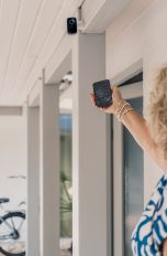 Smart-Home-Security, So schützt du dich vor Hackern Eine Person zeigt mit ihrem Smartphone auf eine smarte Sicherheitskamera vor einer Garage.