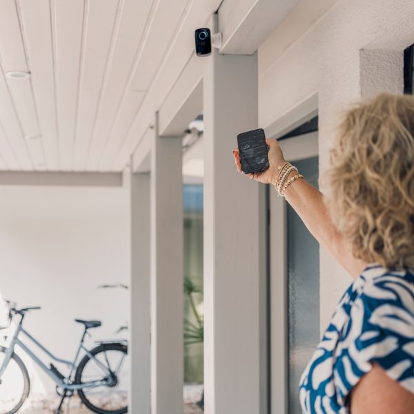 Eine Person zeigt mit ihrem Smartphone auf eine smarte Sicherheitskamera vor einer Garage.
