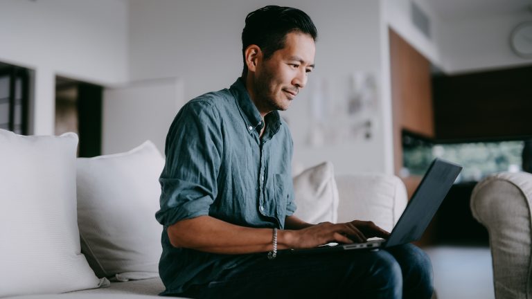 Eine Person sitzt auf einem Sofa und arbeitet an einem Notebook.